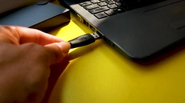 The hand inserts the USB cord into the connector of the laptop. Use of electronic devices at work