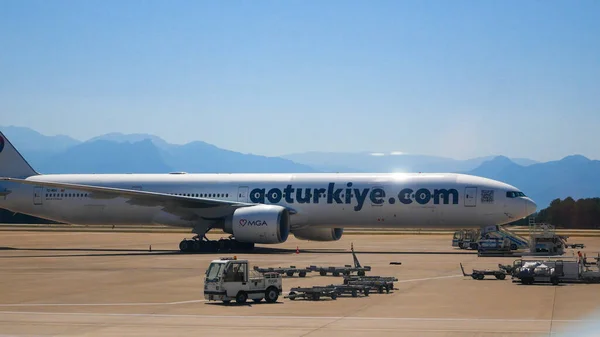 stock image Antalya, Turkey - June, 25, 2023: Plane against the backdrop of mountains at the airport of the resort town. In the foreground are flight maintenance vehicles