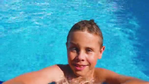 游泳池边可爱的男孩看着摄像机 微笑着回到游泳池里 快乐家庭度假 海上度假的概念 — 图库视频影像