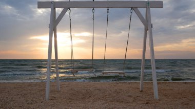 Sabahın erken saatlerinde kumlu bir sahilde beyaz bir salıncak sallanıyor. Güneş denizin üzerinde doğar. Huzur ve sabah meditasyonu kavramı