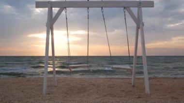 Sabahın erken saatlerinde kumlu bir sahilde beyaz bir salıncak sallanıyor. Güneş denizin üzerinde doğar. Huzur ve sabah meditasyonu kavramı