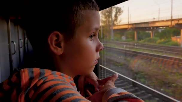 一个坐在火车车厢里的男孩向窗外望去 望着他走过的铁轨和桥 乘火车旅行 铁路客运的概念 — 图库视频影像