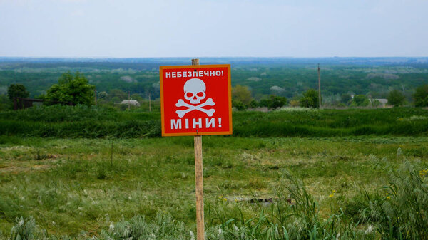 Предупреждающий знак с надписью Осторожно, мины, с изображением черепа на фоне украинской деревни. Горнодобывающие районы после деоккупации украинских сел во время