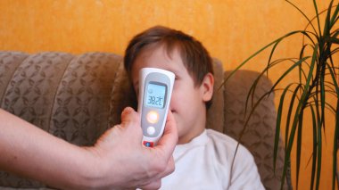 Elektronik termometreyle bir kadının eli bir çocuğun sıcaklığını ölçer. Termometre vücut ısısının yükseldiğini gösteriyor. Evdeki çocuklar için ilk yardım. Evde vücut ısısını ölçüyorum.