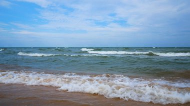 Mavi gökyüzüne karşı kumlu bir sahili olan sakin bir deniz. Köpüklü dalgalar kıyıya vuruyor