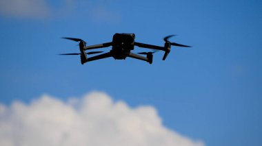 İnsansız hava aracı bulutların arka planında asılı duruyor ve yükseklerden görüntü ve fotoğraf çekiyor. İHA 'nın dönen bıçakları görünür durumda.