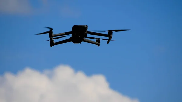 The drone flies in the sky against the background of clouds. The propellers are spinning. The drone is hovering in the sky and conducting surveillance and filming