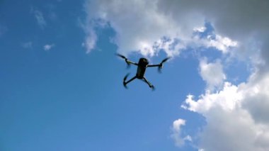 İnsansız hava aracı bulutların arka planında gökyüzünde uçuyor. Pervaneler dönüyor. İnsansız hava aracı gökyüzünde uçuyor ve gözetleme ve çekim yapıyor.