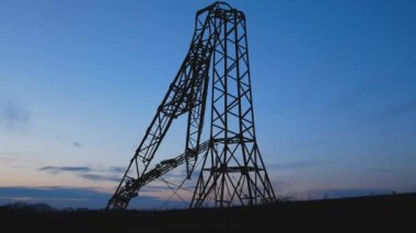 Mavi bir gökyüzünün arka planında yüksek voltajlı elektrik hattının kırık metal direği. Elektrik üretimi ve teslimatı. Enerji güvenliği