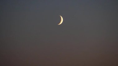 Karanlık gökyüzünde genç bir ay. Ay 'ın, Yeni Ay' dan sonra gökte ilk belirişi dar bir hilal şeklinde..