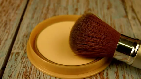 The makeup brush moves over the box of powder. A brush is used to collect makeup powder. Applying powder to the face. Makeup