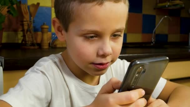 スマートフォンの画面を見て話しているかわいい少年 スマートフォンの助けを借りて通信する ガジェットのゲーム — ストック動画