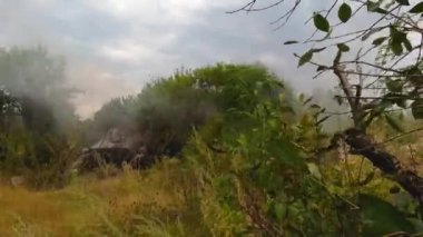 Tankın namlusundan ateş edildiği an. Ağaçların arasında kamufle edilmiş bir tank duruyor. Gerçek bir savaş, bir çatışma. Rus-Ukrayna savaşı.