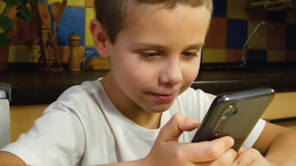 スマートフォンの画面を見て笑顔でかわいい少年 メッセンジャーとのコミュニケーション 距離学習 ガジェットの助けを借りてバーチャル通信 — ストック動画
