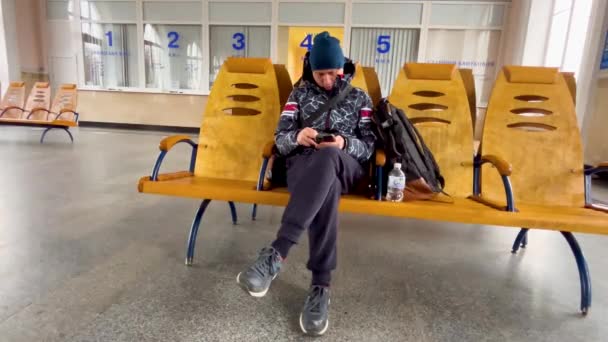 Mężczyzna Plecakiem Siedzi Ławce Pustej Poczekalni Stacji Kolejowej Mężczyzna Patrzy — Wideo stockowe