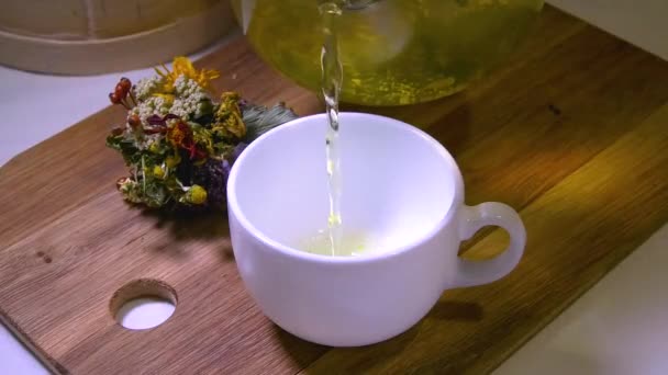将清澈的茶壶中的草药茶倒入白杯中 附近有一束草本植物 草药茶 健康生活方式概念 — 图库视频影像