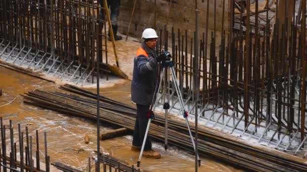 乌克兰哈尔科夫 2023年12月4日 一位建筑商站在金属加固中的水泥地基上 看着测量装置并设定水平仪 工程的建造 — 图库视频影像