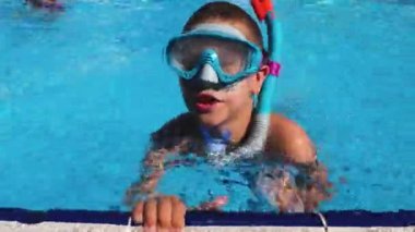 Yüzme gözlüğü takan ve şnorkel takan bir çocuk mavi bir su havuzunun kenarına kadar yüzer. Suda yaz tatili. Tatiller ve çocuklar için rehabilitasyon.