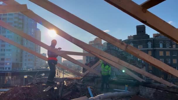 ウクライナのハリコフ 2023年11月30日 建築家が木製のハンマーの爪の屋根の上に立っています 屋根の修理 背景には大きな建物の複数の階建ての建物があります — ストック動画