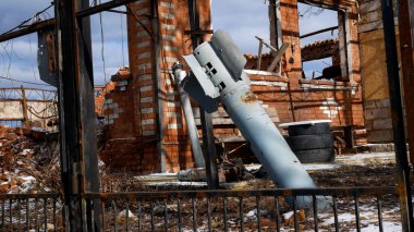 A projectile from a Grad multiple launch rocket system got stuck in the ground against the background of a destroyed residential building in a Ukrainian village. Shelling of peaceful villages. A clipart