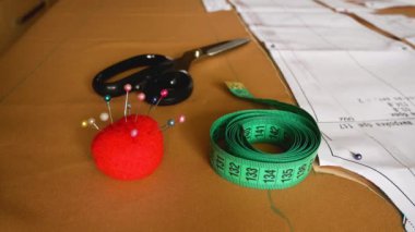 Dikiş aksesuarları: makas, bir santimetre ve bir iğne tutacağı kesim masasında kumaşa bağlı desenlerin yanında. Kumaş kesmek, dikiş ürünleri. Hobi olarak. Modelleme ve üretim