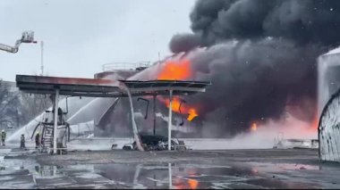 Petrol deposunda yangın. Petrol ürünleriyle tankları yakmak. Büyük duman ve ateş bulutları püskürdü. Güçlü su püskürtüleri yangını söndürür..