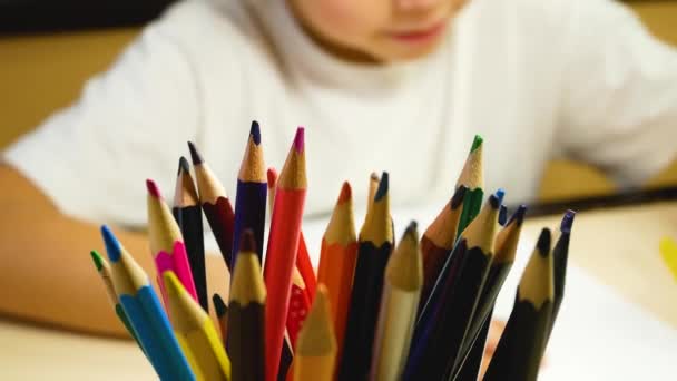 一个5 6岁的男孩用纸上的铅笔勤奋地画画 前面是一个有铅笔的杯子 — 图库视频影像