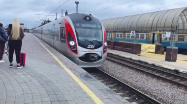 Kharkiv, Ukrayna - Aralık 04, 2023: Şehirlerarası bir tren yavaşça tren istasyondaki platforma yanaşır. Yolcular platformda duruyor. Yolcu için yüksek hızlı trenler