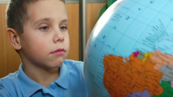 소년은 지구를 조심스럽게 바라보고 회전시키고 국가와 지리학을 공부합니다 학교에서 지리학 — 비디오
