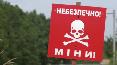 Üzerinde yazı olan bir kırmızı uyarı işareti yeşil bir ormanın arka planında mayınlanır. İnsani mayın temizleme kavramı. Düşmanlığın sonuçlarına katlanmak. Rus-Ukrayna savaşı.