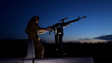 Kharkiv, Ukrayna - 27 Şubat 2024: Bir asker bir cipin arkasında duruyor, gece gökyüzüne bakıyor ve makineli tüfekle nişan alıyor. Ordu bir İHA arıyor, gökyüzünde bir İHA.