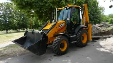 Kharkiv, Ukrayna - Haziran 08, 2024: Kovalı bir kazıcı, kazıcı kovası tarafından kazılan bir çukurun yanındaki iş yerine gidiyor. Toprak hareket makineleriyle onarım çalışmaları.