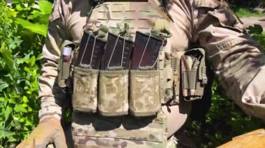 Askeri kamuflaj üniformalı, kurşun geçirmez yelek giyen, göğsünde yedek kartuşlar için boynuzları olan bir savaşçı. Savaşçı, savaşta olan bir asker. Gerçek bir savaş. Rus-Ukrayna savaşı, seferberlik.