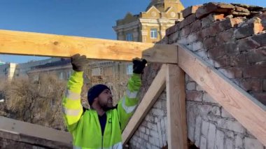 Kharkiv, Ukrayna - 30 Kasım 2023: Bir işçi çatıyı tamir eder, çatıya bir kiriş, bir kiriş yerleştirir. Arka planda büyük bir şehrin çok katlı binaları var. Eskinin yeniden inşası