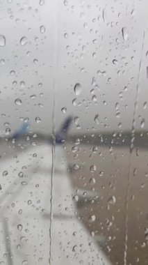 Yağmur damlalarının aktığı bir pencere. Arka planda, uçağın kanadı pencereden görülebilir. Yağmurda uçak uçurmak. Uçmayan hava.