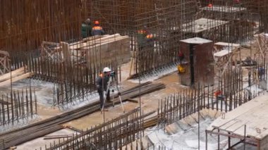 Kharkiv, Ukrayna - Aralık 04, 2023: İnşaat alanı. Bir müteahhit ölçüm cihazına bakar, diğerleri demir takviyesi giyer..