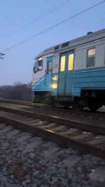 Pencerelerinde ışıklar olan bir yolcu treni akşamları demiryolu ile seyahat eder. Banliyö yolcu taşımacılığı.