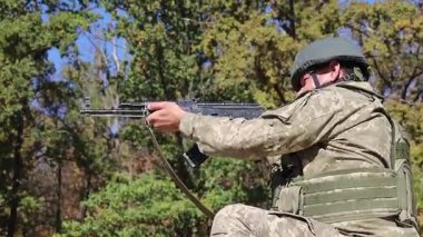 Askeri teçhizatlı bir piyade askeri, bir kask ve kurşun geçirmez yelek, çömelmiş ve Kalaşnikof saldırı tüfeğiyle ateş ediyor. Şehir savaşları. Gerçek savaş..