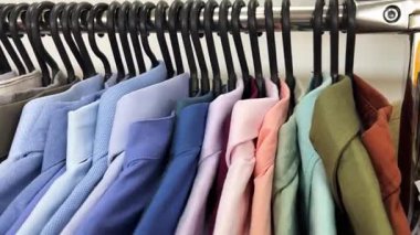 Birçok renkli erkek gömleği bir giyim mağazasında askılarda asılı duruyor. Sıradan ya da resmi kıyafetler için erkek modası ve alışveriş seçimi. Erkek gardırobu.
