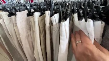 Bir kadın, mağazadaki askılara asılan pantolonları elden ele ayırır. Satış sırasında kıyafet al. Gardırop düzeni. Mağazada bir sürü kıyafet var. İkinci el giyim konsepti.