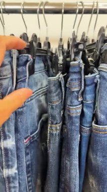 Bir kadın, giyim mağazasında askılarda asılı olan kotları sınıflandırır. Alışveriş süreci, kostüm seçimi ve günlük moda..