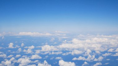 Scattered small white clouds seen from above through an airplane window. Bright blue sky and peaceful aerial atmosphere.