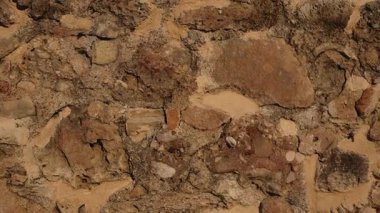 Büyük ve küçük taşlardan yapılmış desenli kahverengi taş duvar. Taşların arasında görünen kilden bir yapı. Kadim yapı malzemesi arka planı.