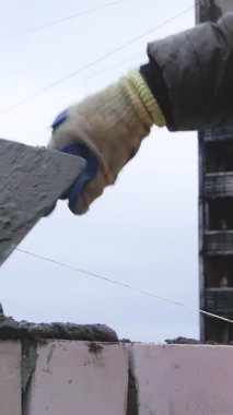 İşçi elinde bir tuğla tutuyor, çimentoya koyuyor, evin duvarını inşa ediyor. Rus bombardımanından sonra Ukrayna şehrinin restorasyonu. Konut