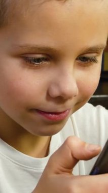 Mutfakta elinde telefon olan 6-7 yaşlarında bir çocuk. Çocuk ekranda parşömen çiziyor, konuşuyor. Cihazların yardımıyla sosyal ağlarda iletişim. Çocuklar ve aletler. Elektronik oyunlar.