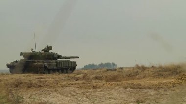 Bir tank kumlu arazide namlusu bir hedefe doğrultulmuş vaziyette duruyor. Savaş sırasında ağır zırhlı araçların çarpışmaya hazır olması. Russo-Ukrayna savaşı.