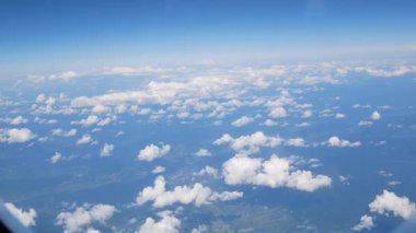 Beyaz sirrus bulutları mavi gökyüzünde süzülür, bir uçak penceresinden hava manzarası. Hafiflik, seyahat, huzurlu gökyüzü.