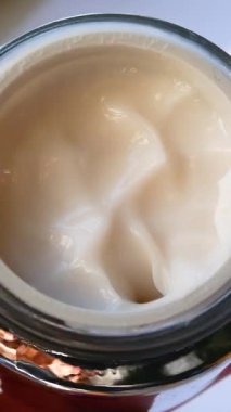 Bir kadının eli bir krem kavanozunu açar, parmağıyla beyaz yüz kremi sürmeye çalışır. Cilt bakımı, yaşlanmayı önleyen güzellik tedavileri. Kozmetik prosedürleri.