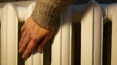 Bir kadının eli radyatöre dokunur ve odadaki ısıyı kontrol eder. Isınma mevsiminin başlaması, ev ısıtma konsepti, bir apartman dairesinde veya evde enerji kullanımı.