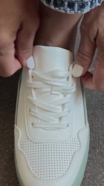 Kadın eli, ayakkabı bağcıklarını beyaz spor ayakkabılara bağlar. Spor ve eğlence için rahat ayakkabılar konsepti. Rahat rahat ayakkabılar..